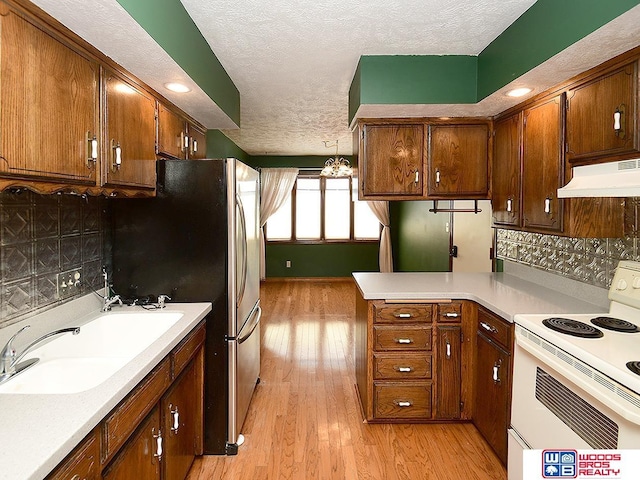 kitchen with light wood finished floors, tasteful backsplash, electric range, light countertops, and under cabinet range hood