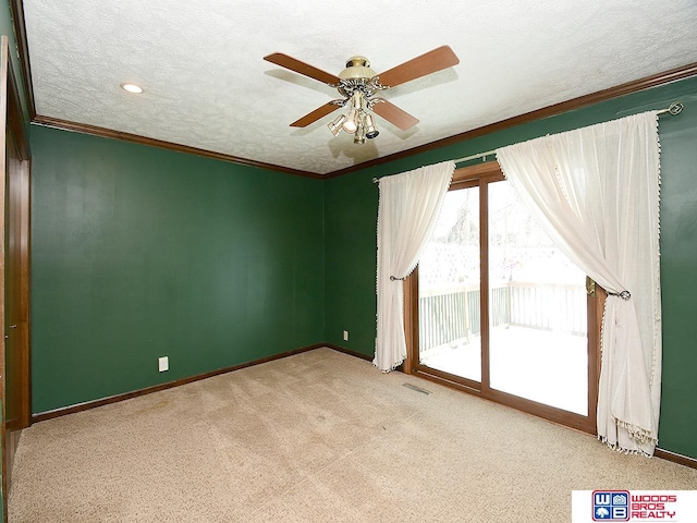carpeted spare room featuring a textured ceiling, a ceiling fan, visible vents, baseboards, and ornamental molding