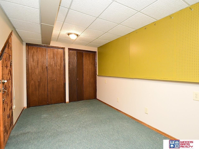 unfurnished bedroom featuring a drop ceiling, carpet, two closets, and baseboards