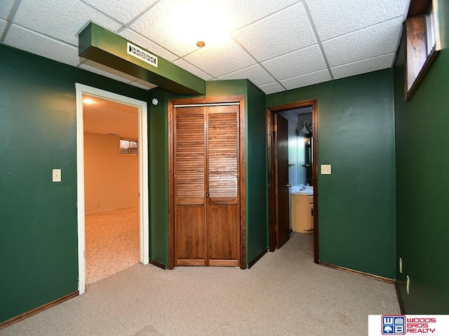 hallway featuring baseboards, a drop ceiling, and light colored carpet
