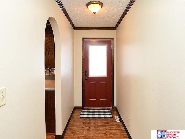 entryway featuring a textured ceiling, arched walkways, wood finished floors, baseboards, and ornamental molding