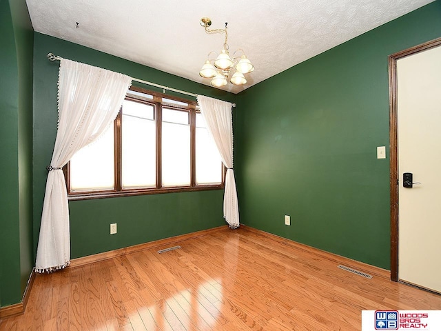 unfurnished room featuring a chandelier, a textured ceiling, light wood-type flooring, and visible vents