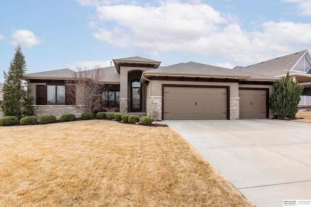 prairie-style house with a garage, stone siding, a front yard, and stucco siding