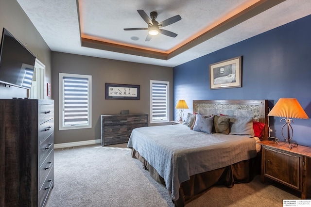 carpeted bedroom featuring a raised ceiling, ceiling fan, a textured ceiling, and baseboards