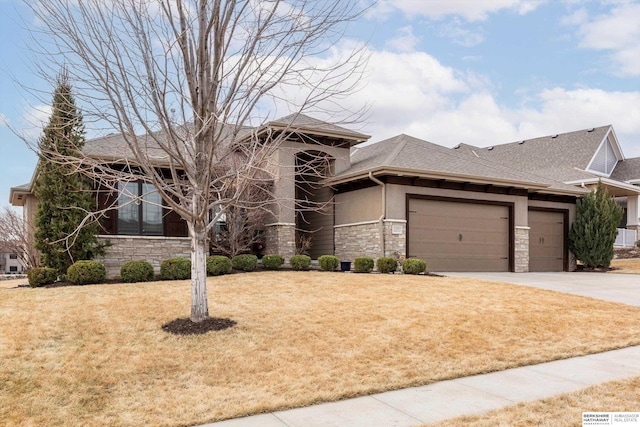 prairie-style home featuring a front yard, stone siding, an attached garage, and concrete driveway