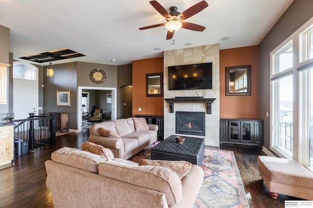 living room with dark wood-style floors, a tiled fireplace, a wealth of natural light, and baseboards