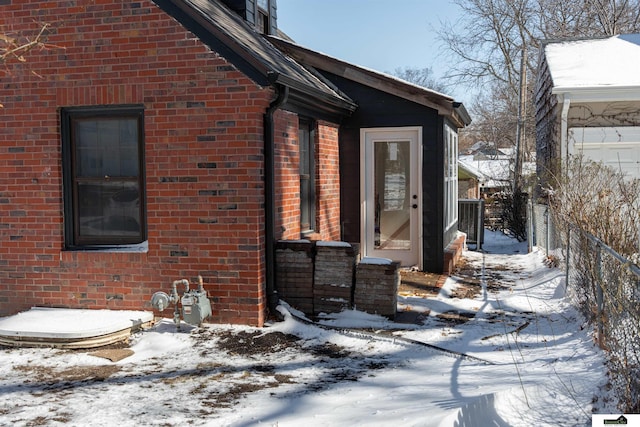 view of snow covered exterior featuring brick siding and fence