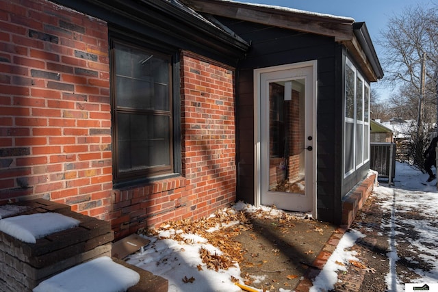 snow covered property entrance with brick siding