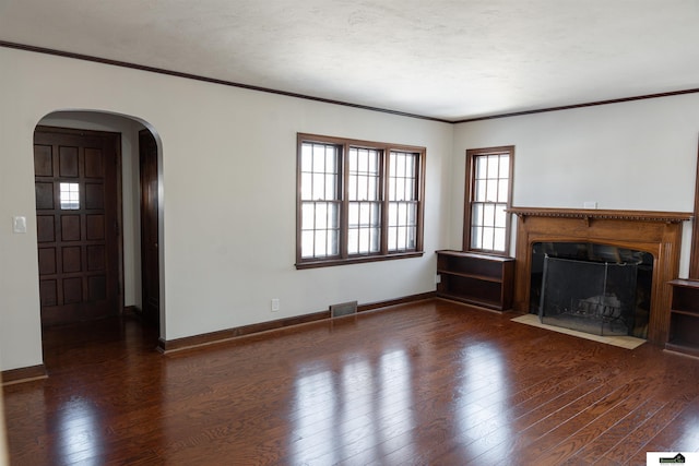 unfurnished living room with arched walkways, hardwood / wood-style flooring, visible vents, baseboards, and ornamental molding