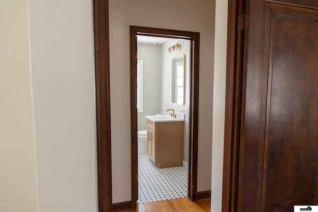 hallway with light wood-type flooring, baseboards, and a sink