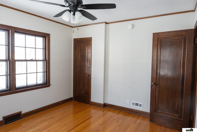 unfurnished bedroom featuring light wood-type flooring, baseboards, visible vents, and crown molding