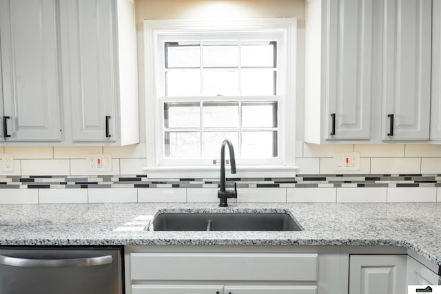 kitchen with tasteful backsplash, dishwasher, a sink, and light stone countertops