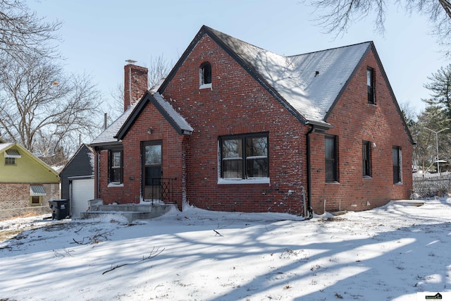 tudor-style house with brick siding, a detached garage, and a chimney