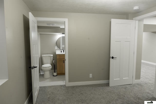 carpeted bedroom with a textured ceiling, baseboards, and ensuite bathroom