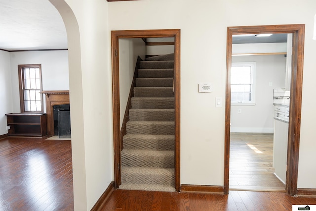 staircase with a fireplace with flush hearth, arched walkways, baseboards, and hardwood / wood-style floors