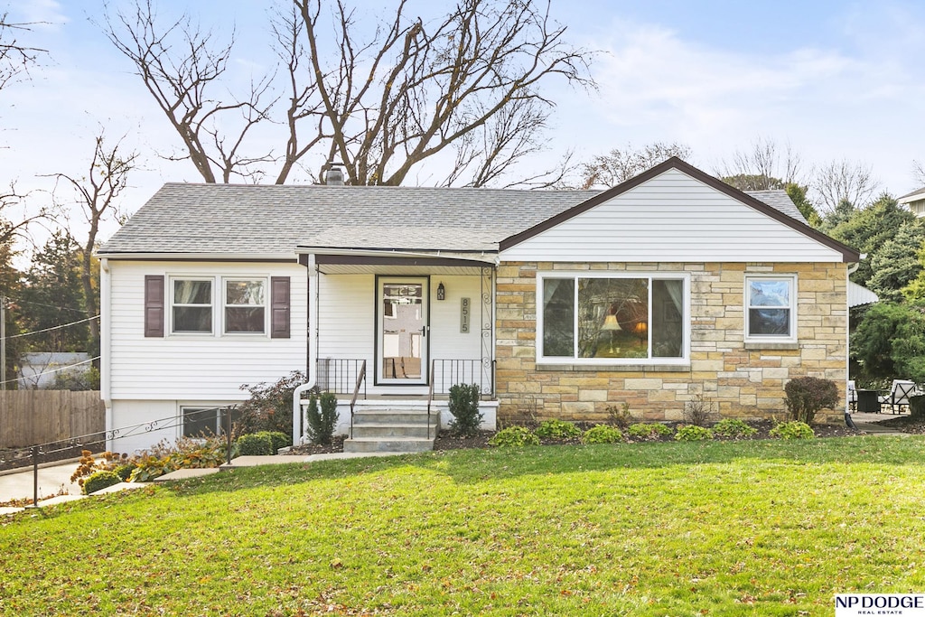 view of front of home with stone siding, roof with shingles, fence, and a front yard