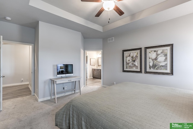 carpeted bedroom featuring ceiling fan, visible vents, baseboards, a raised ceiling, and ensuite bath