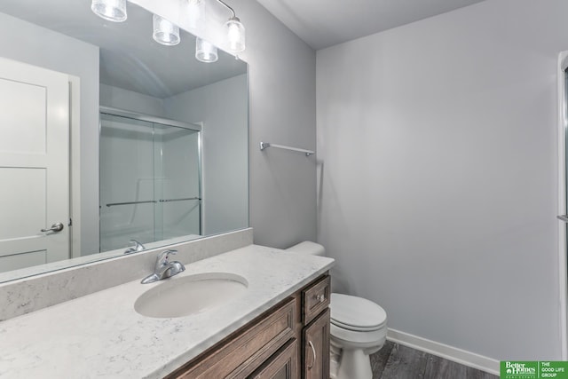 bathroom with toilet, a shower with shower door, wood finished floors, vanity, and baseboards