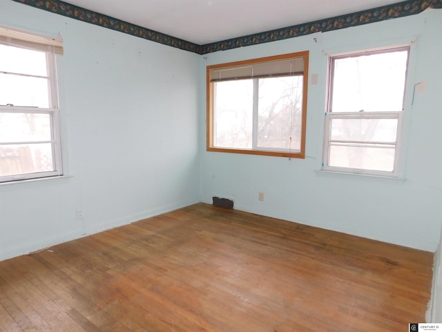 unfurnished room with light wood-type flooring, visible vents, plenty of natural light, and baseboards