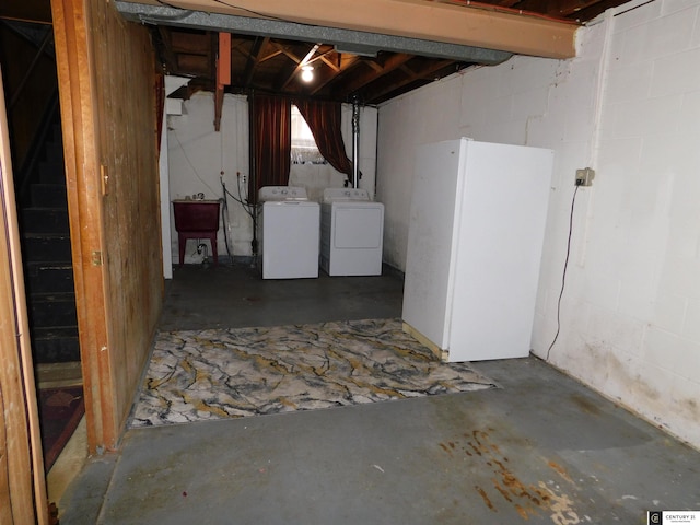 unfinished below grade area featuring concrete block wall, a sink, freestanding refrigerator, and washer and dryer