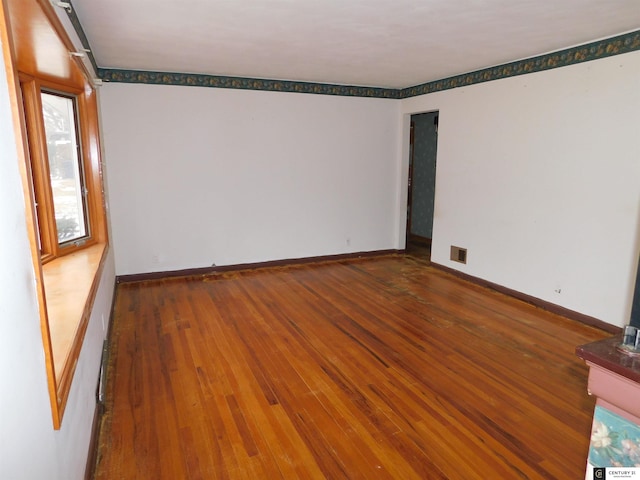 empty room with hardwood / wood-style flooring, visible vents, and baseboards