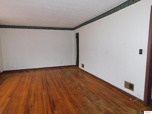 unfurnished room featuring wood-type flooring, visible vents, and baseboards