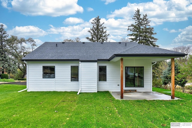 rear view of property with roof with shingles, a patio, and a lawn