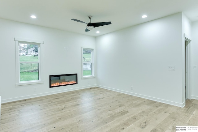 unfurnished living room featuring light wood-style flooring, recessed lighting, a ceiling fan, baseboards, and a glass covered fireplace