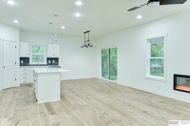 kitchen with a kitchen island, light wood-style floors, white cabinets, light countertops, and decorative backsplash