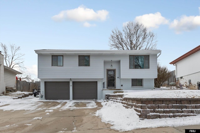 raised ranch with an attached garage, fence, and brick siding