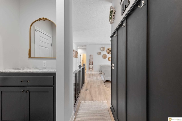 corridor featuring light wood-style floors, a textured ceiling, and baseboards