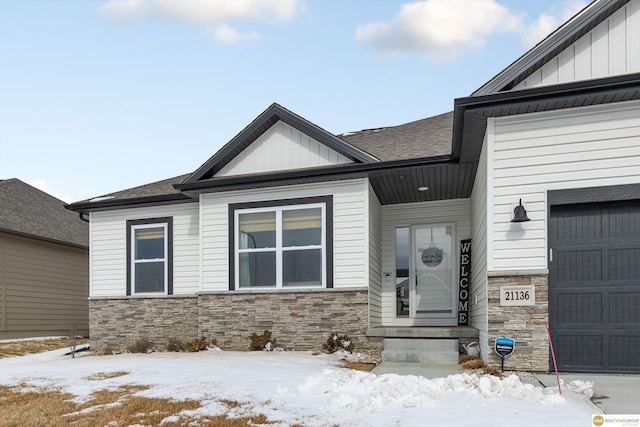 view of front of home with a garage, stone siding, board and batten siding, and roof with shingles