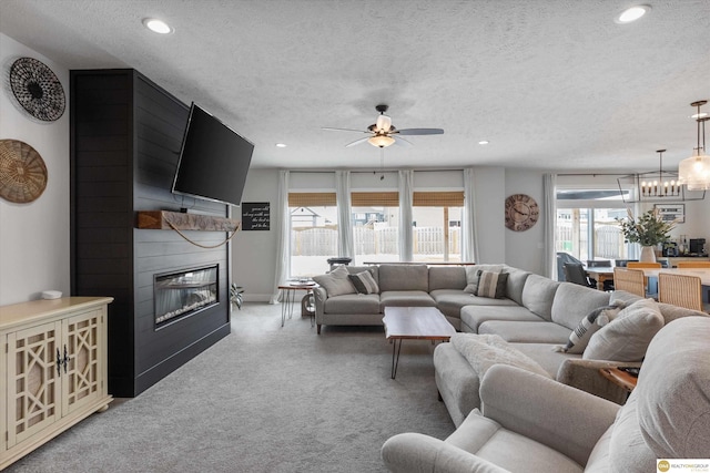 living area featuring light carpet, recessed lighting, a textured ceiling, a fireplace, and ceiling fan with notable chandelier