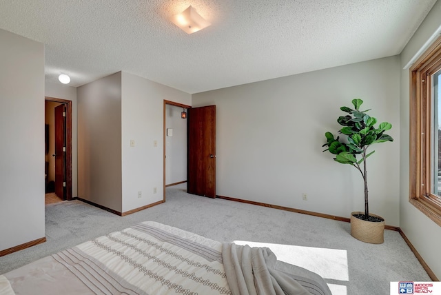 bedroom with light colored carpet, a textured ceiling, and baseboards