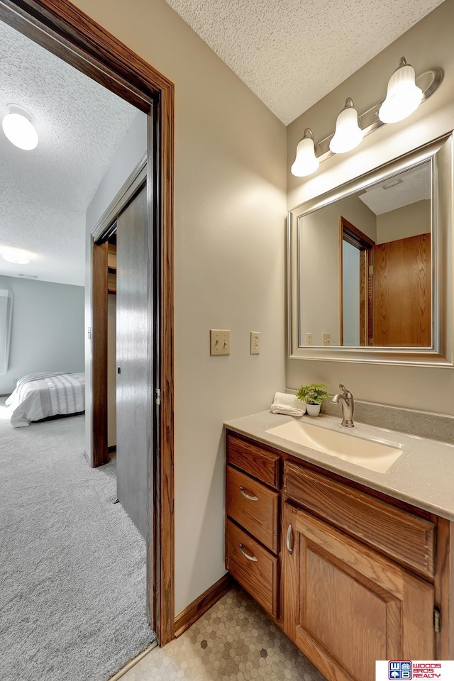 bathroom with a textured ceiling, ensuite bathroom, vanity, and baseboards