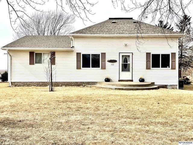 back of house with roof with shingles and a lawn