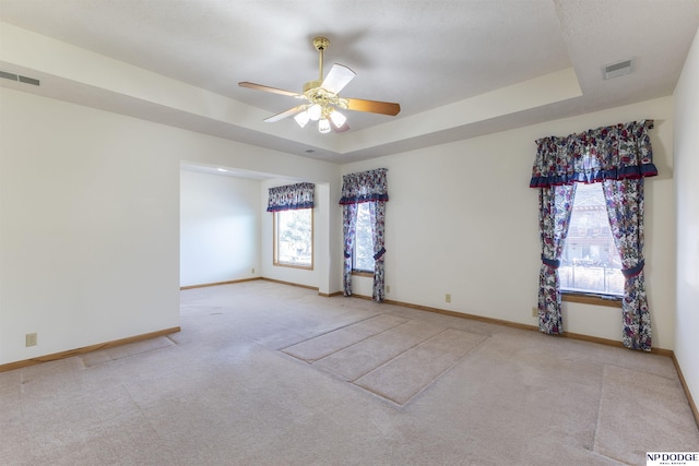 unfurnished room featuring a tray ceiling, carpet flooring, visible vents, and baseboards