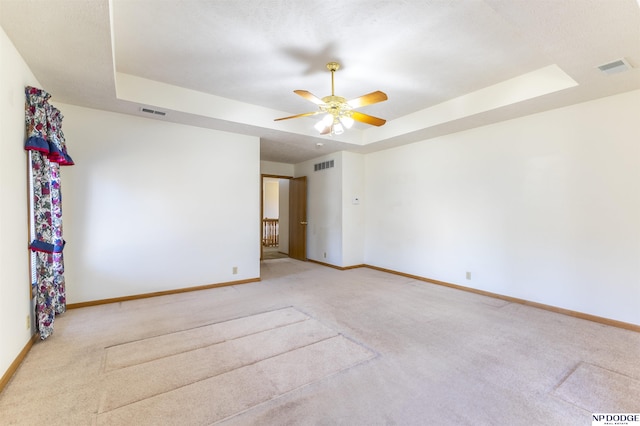 carpeted spare room featuring a tray ceiling, visible vents, ceiling fan, and baseboards