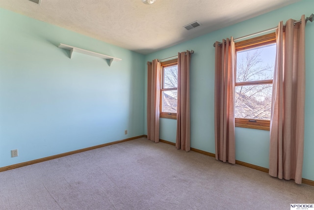 empty room featuring light carpet, baseboards, visible vents, and a textured ceiling