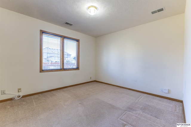 spare room featuring a textured ceiling, carpet floors, visible vents, and baseboards