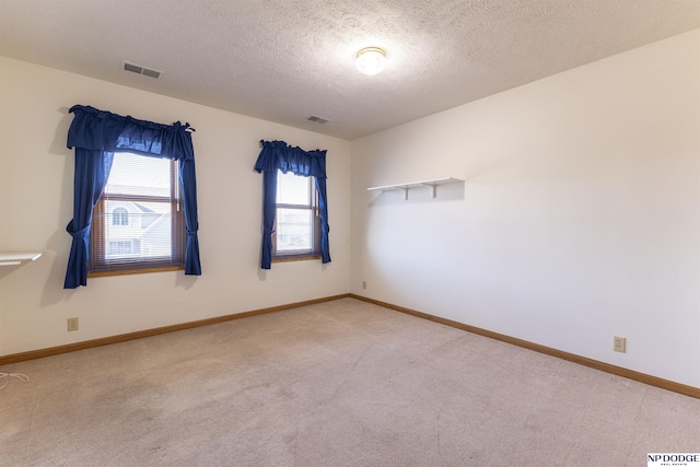 spare room with a textured ceiling, carpet floors, visible vents, and baseboards