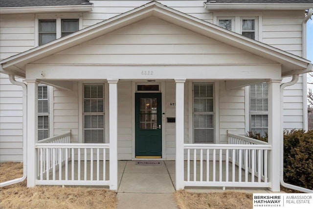 entrance to property with a porch and roof with shingles