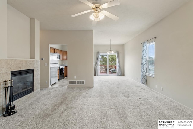 unfurnished living room with ceiling fan with notable chandelier, a tiled fireplace, visible vents, and light colored carpet