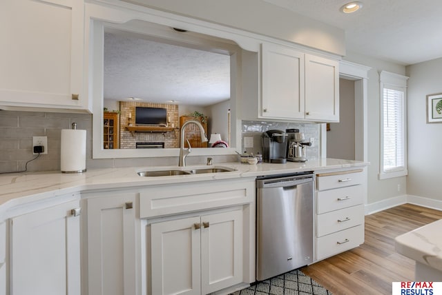 kitchen featuring stainless steel dishwasher, a sink, white cabinets, and light wood-style floors