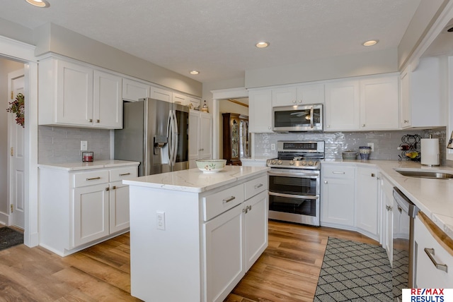 kitchen with a center island, stainless steel appliances, white cabinets, a sink, and light wood-type flooring