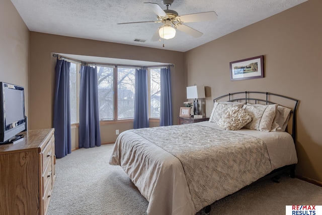 bedroom with light carpet, a textured ceiling, visible vents, and a ceiling fan