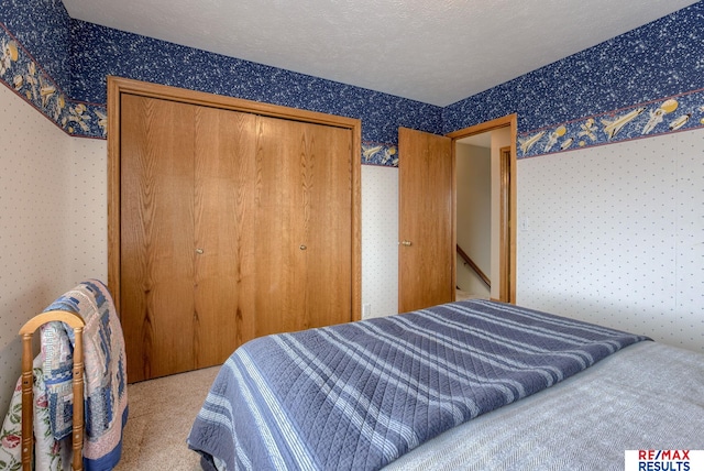 bedroom featuring carpet floors, wallpapered walls, a closet, and a textured ceiling