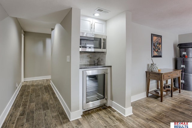 bar with a dry bar, beverage cooler, visible vents, stainless steel microwave, and dark wood-type flooring