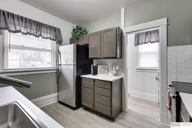 kitchen with light countertops, light wood finished floors, freestanding refrigerator, and a healthy amount of sunlight