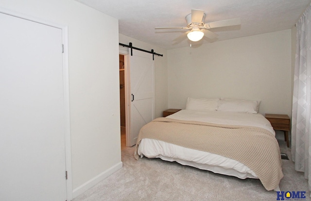 carpeted bedroom with ceiling fan, a barn door, and baseboards